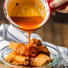 Pouring buffalo sauce on freshly fried wings